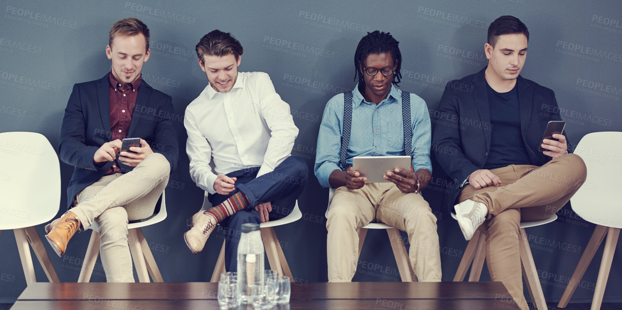 Buy stock photo Shot of a group of businessmen using different wireless devices while waiting in line for an interview