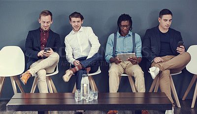 Buy stock photo Shot of a group of businessmen using different wireless devices while waiting in line for an interview