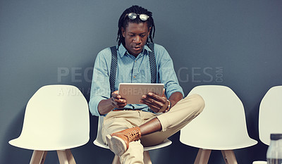 Buy stock photo Shot of a young businessman using a tablet while waiting for an interview