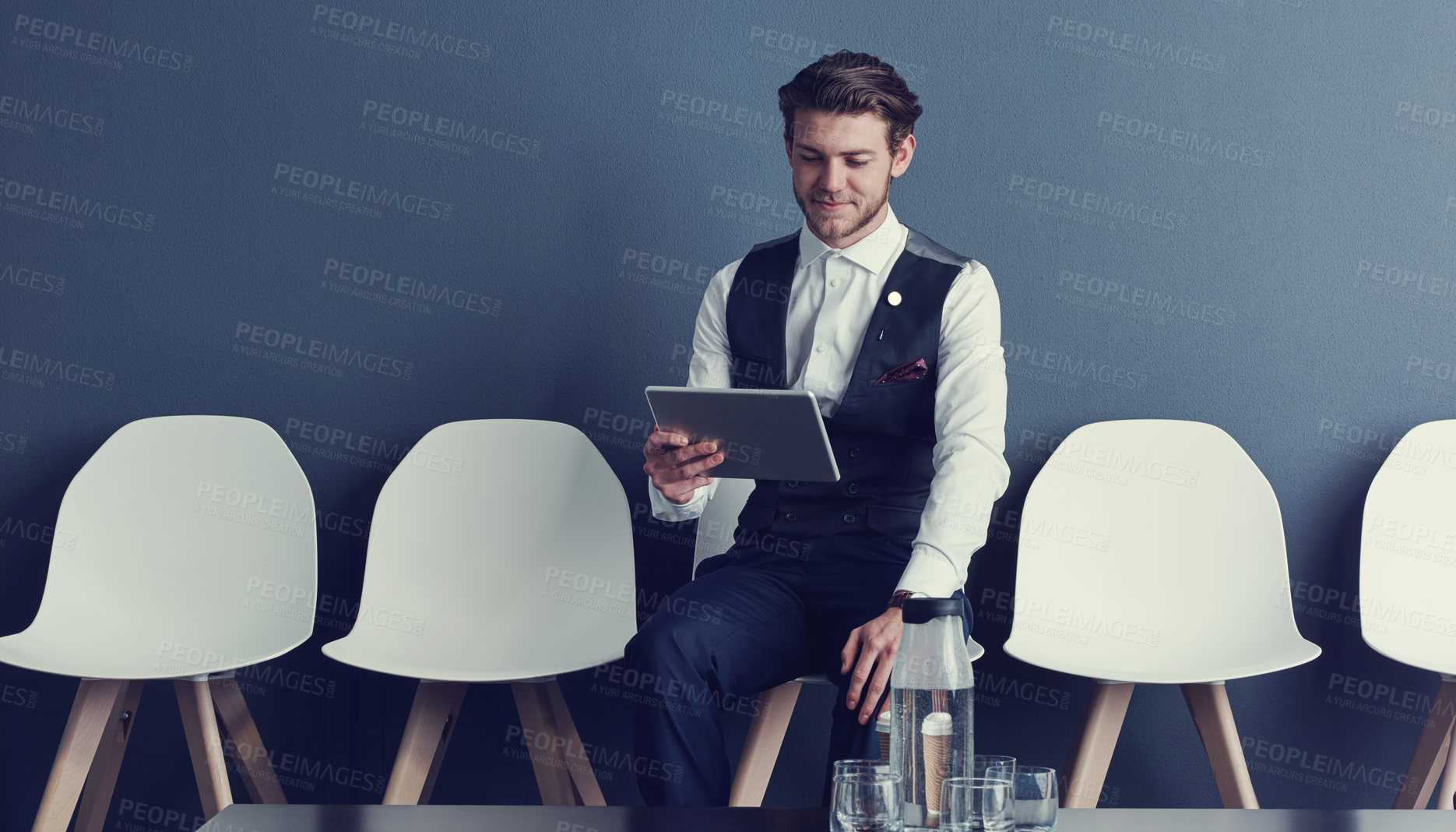 Buy stock photo Shot of a young businessman using a tablet while waiting for an interview