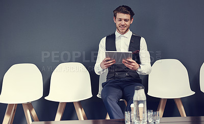 Buy stock photo Shot of a young businessman using a tablet while waiting for an interview