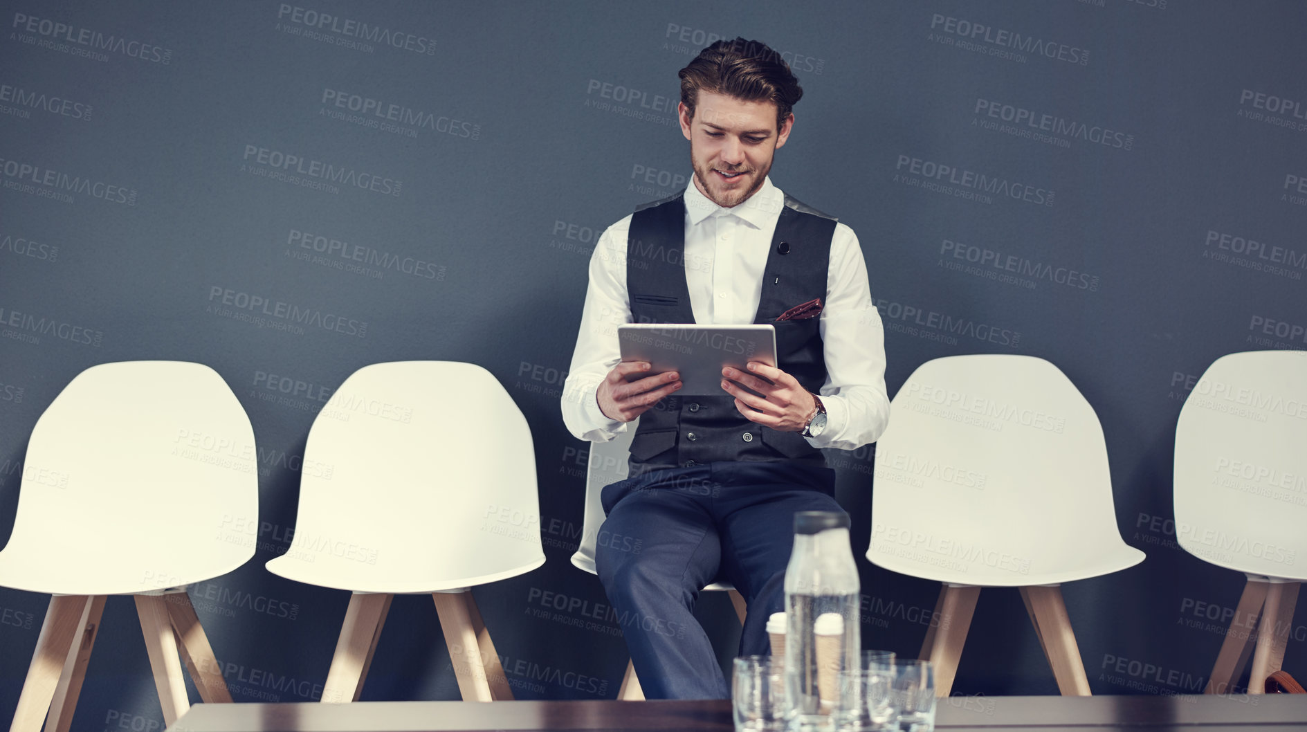 Buy stock photo Shot of a young businessman using a tablet while waiting for an interview