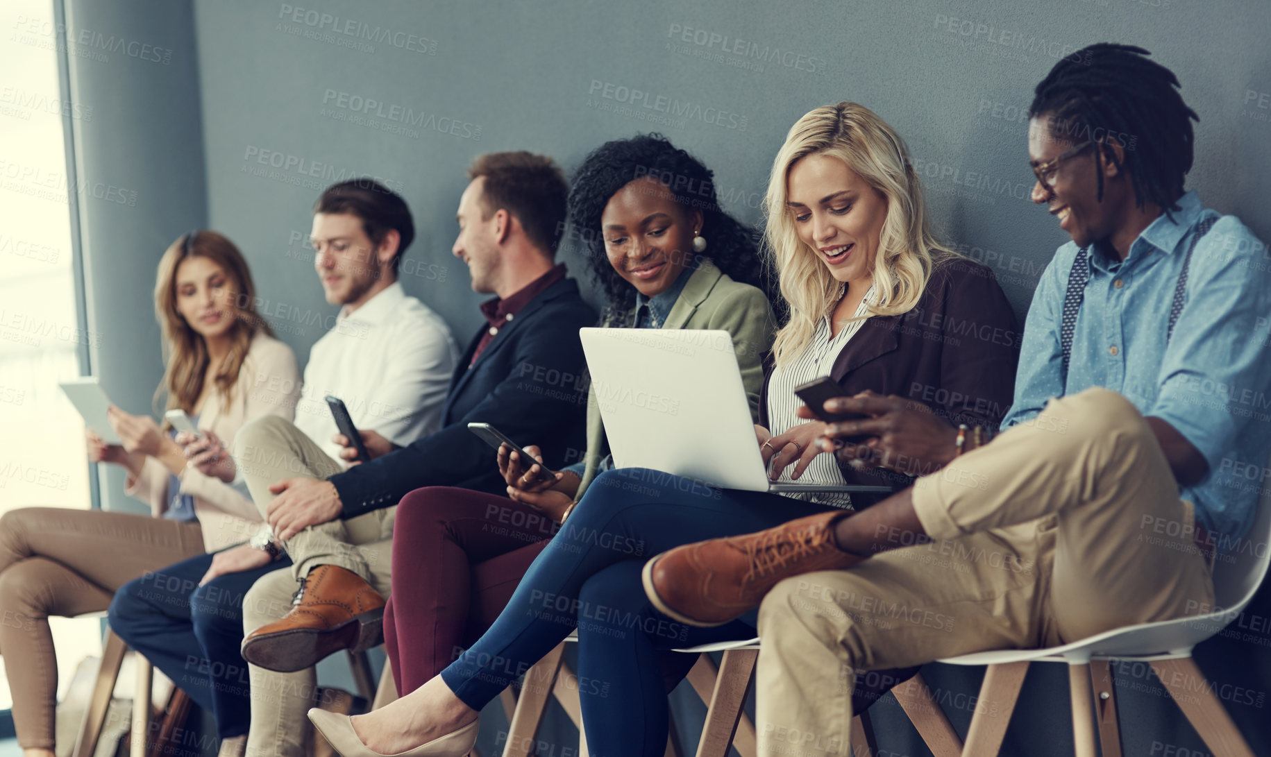 Buy stock photo Shot of a group of businesspeople using different wireless devices while waiting in line for an interview