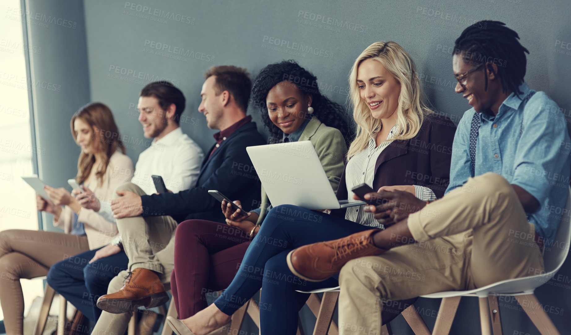 Buy stock photo Shot of a group of businesspeople using different wireless devices while waiting in line for an interview