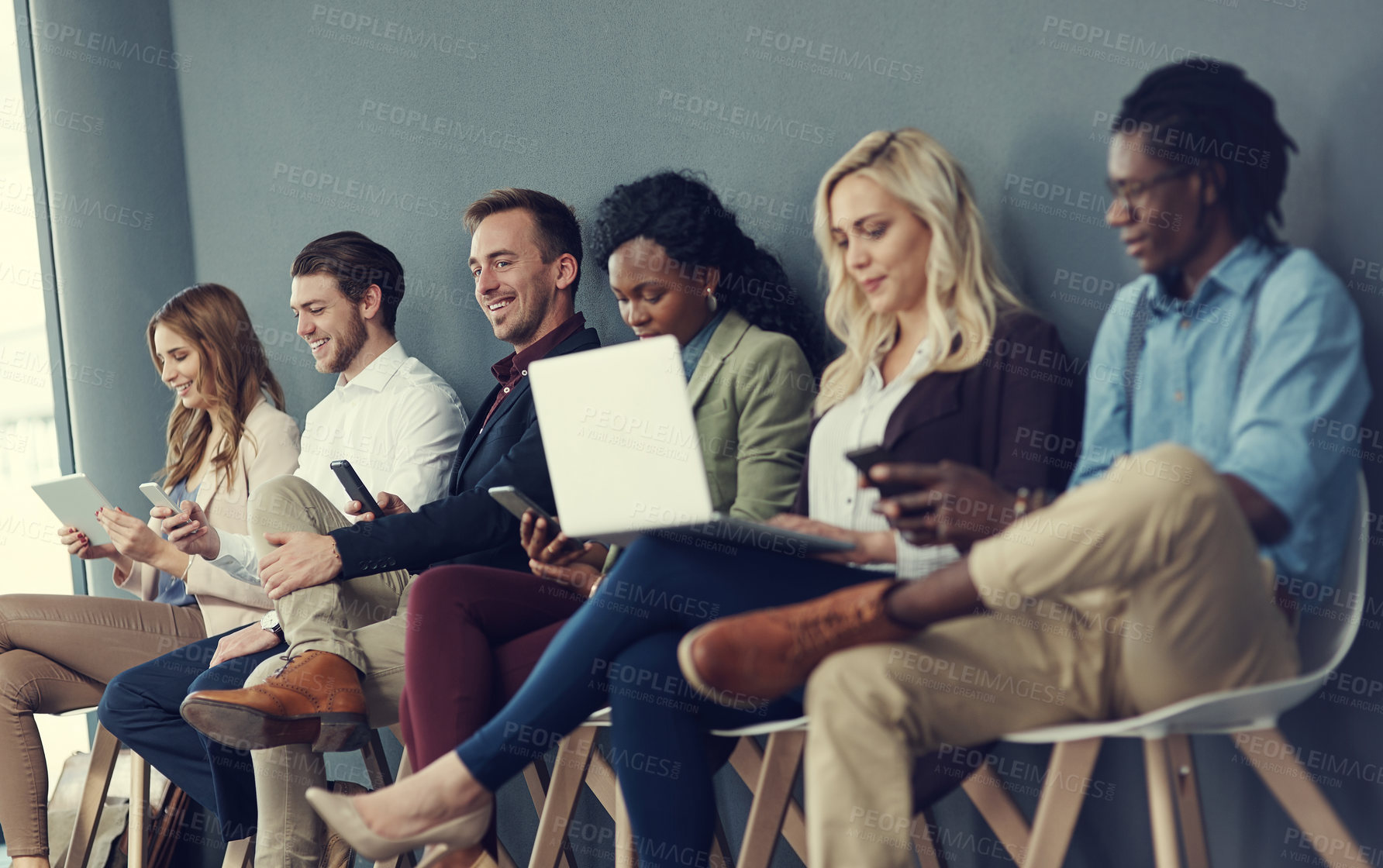 Buy stock photo Shot of a group of businesspeople using different wireless devices while waiting in line for an interview