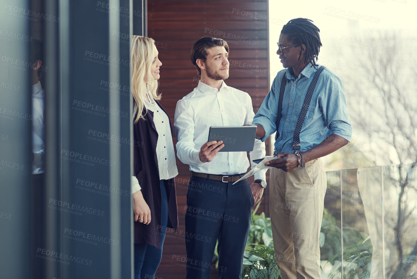 Buy stock photo Cropped shot of three young businesspeople using a tablet while standing outside on the office balcony