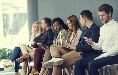 Buy stock photo Shot of a group of businesspeople using different wireless devices while waiting in line for an interview