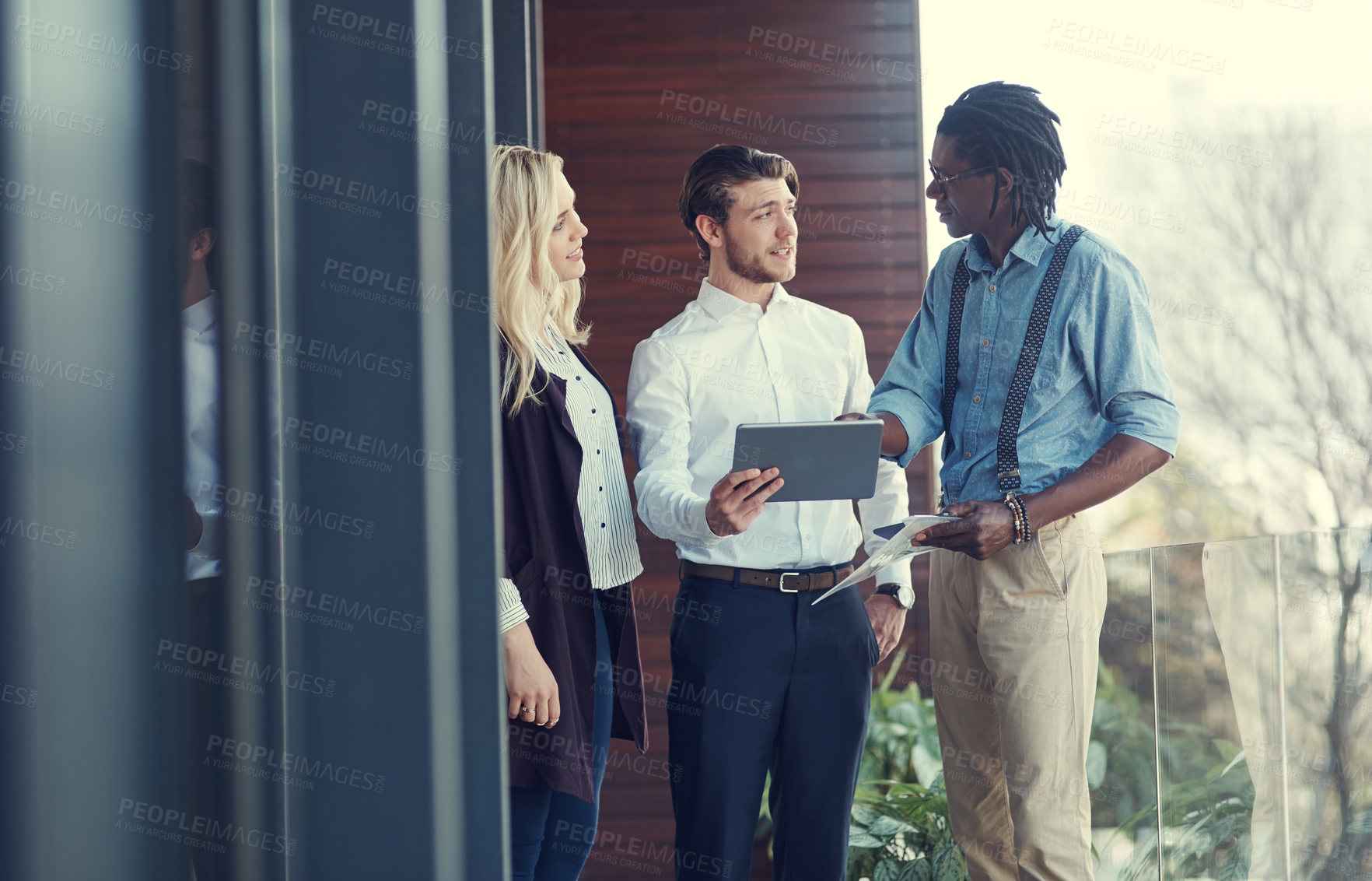 Buy stock photo Cropped shot of three young businesspeople using a tablet while standing outside on the office balcony