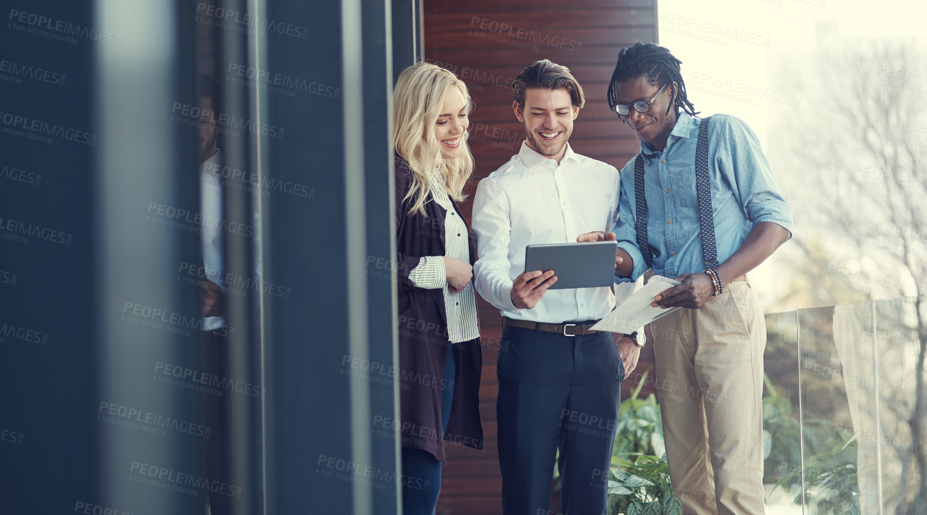 Buy stock photo Cropped shot of three young businesspeople using a tablet while standing outside on the office balcony