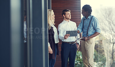 Buy stock photo Cropped shot of three young businesspeople using a tablet while standing outside on the office balcony