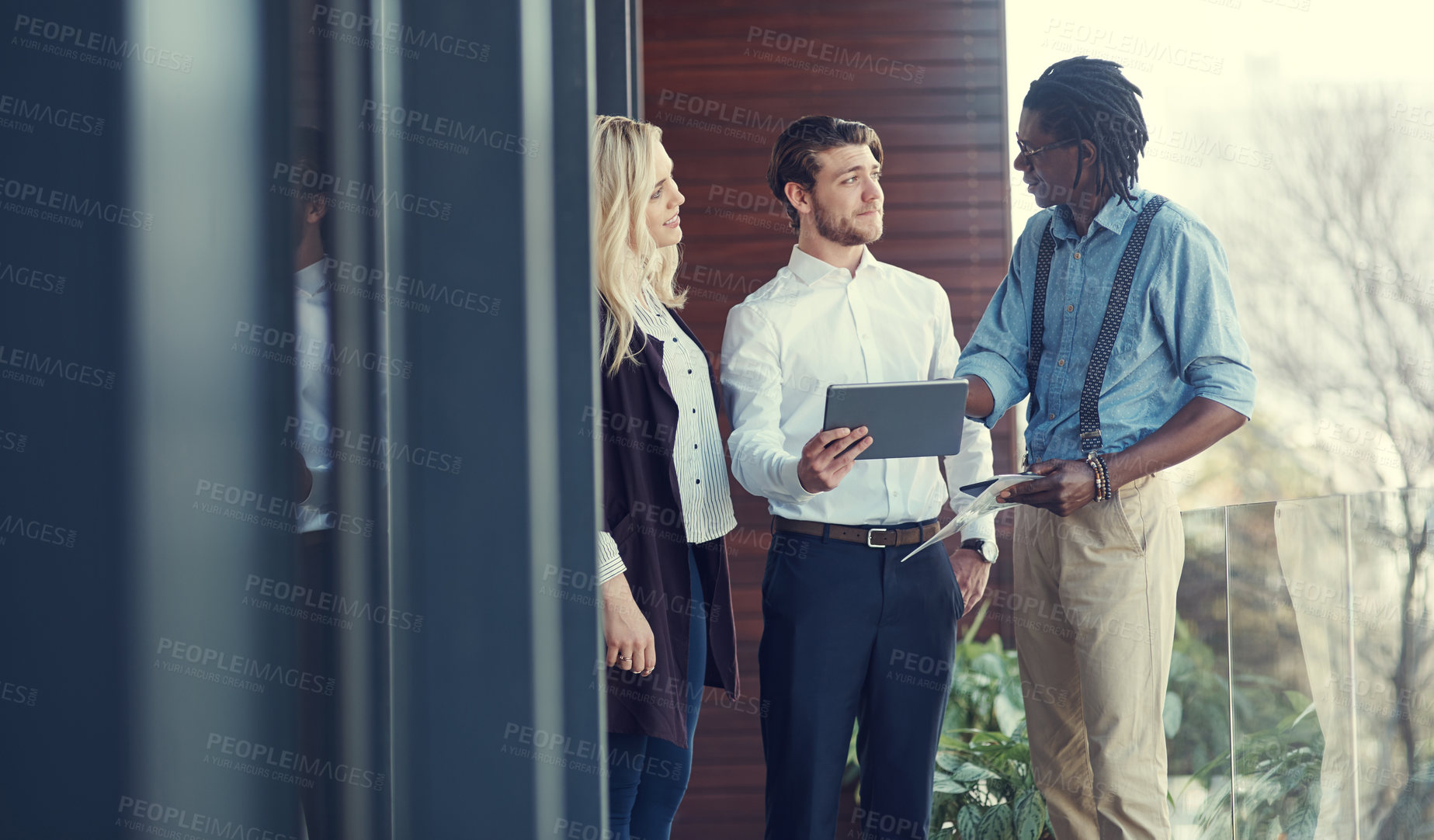 Buy stock photo Cropped shot of three young businesspeople using a tablet while standing outside on the office balcony