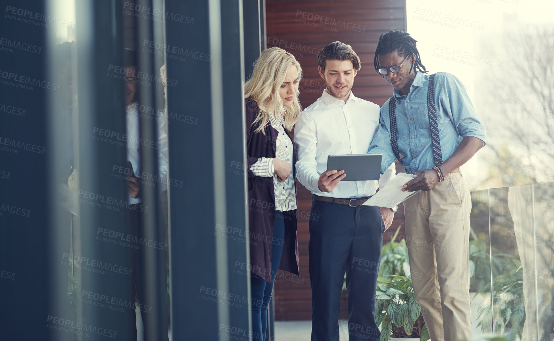 Buy stock photo Cropped shot of three young businesspeople using a tablet while standing outside on the office balcony