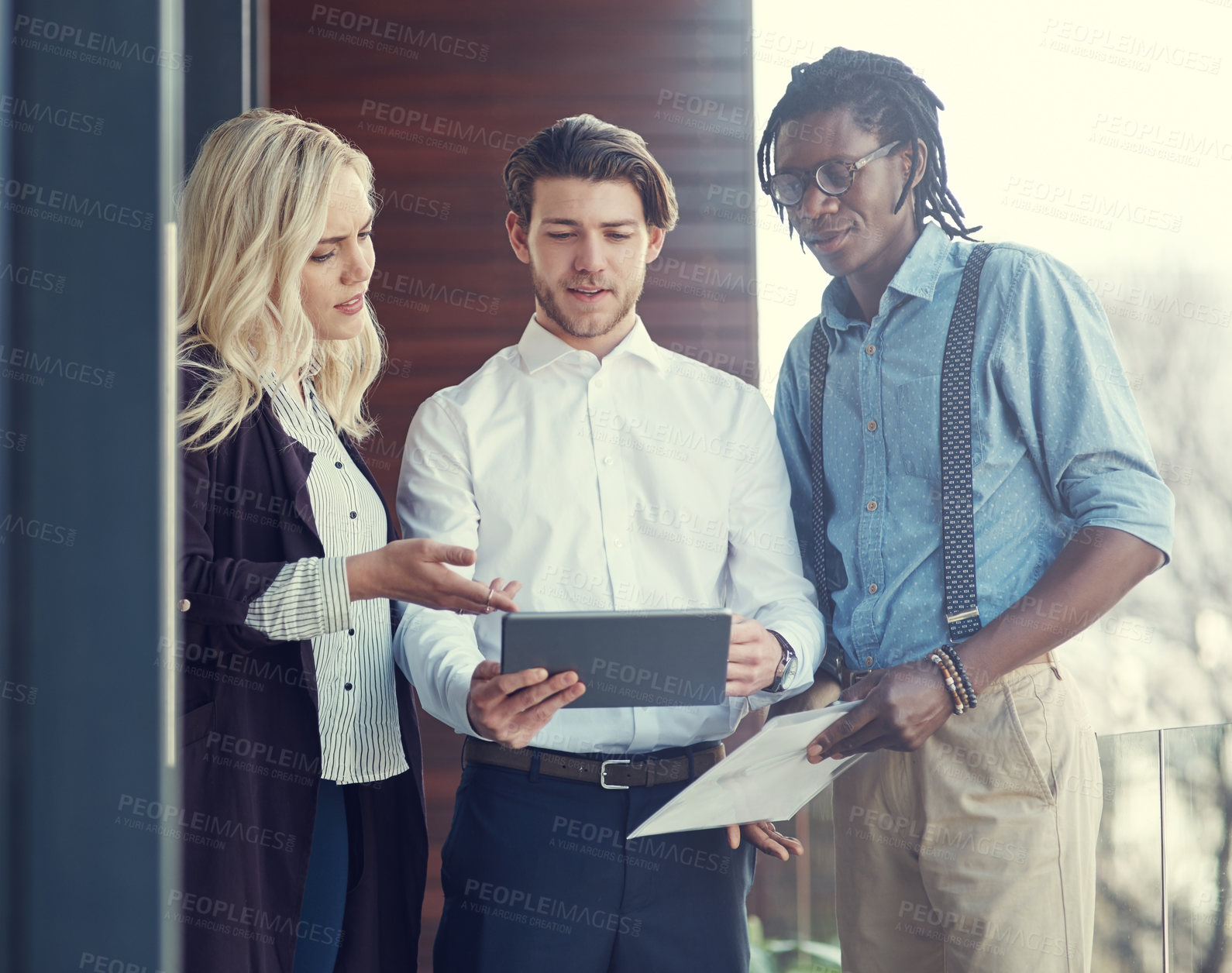 Buy stock photo Cropped shot of three young businesspeople using a tablet while standing outside on the office balcony