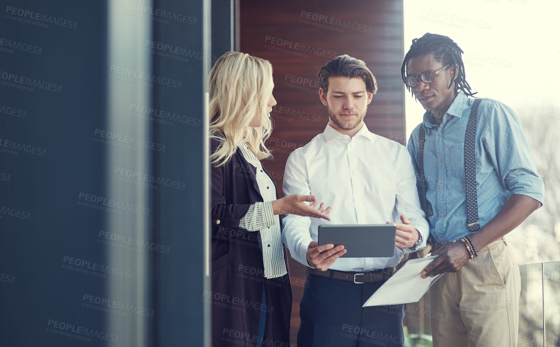 Buy stock photo Cropped shot of three young businesspeople using a tablet while standing outside on the office balcony