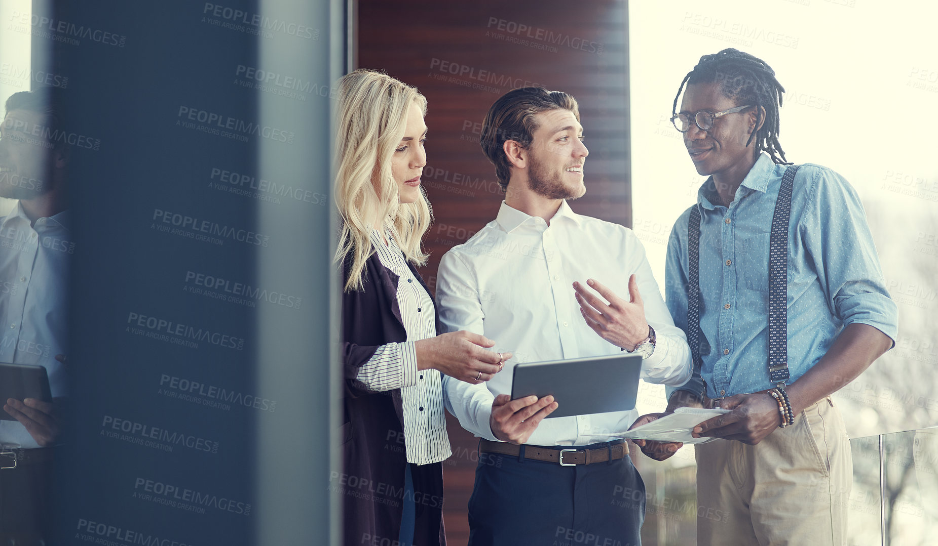 Buy stock photo Cropped shot of three young businesspeople using a tablet while standing outside on the office balcony
