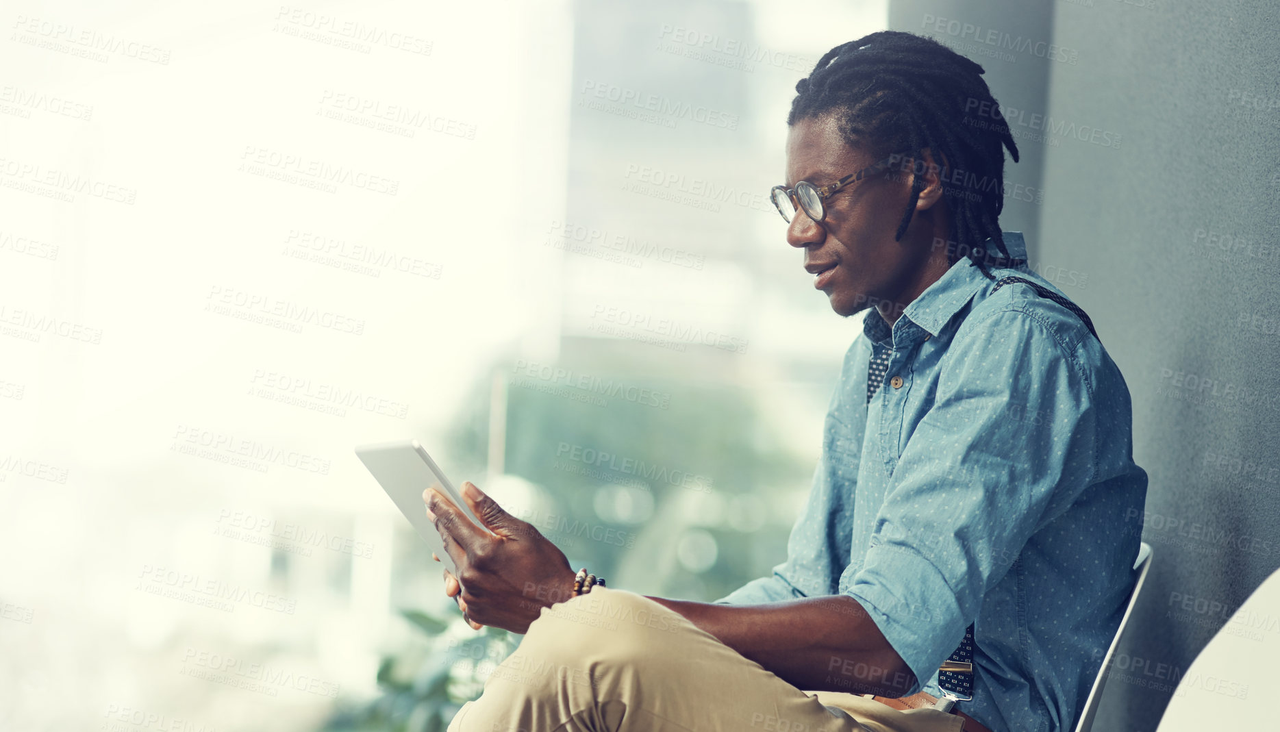 Buy stock photo Shot of a young businessman using a tablet while waiting for an interview