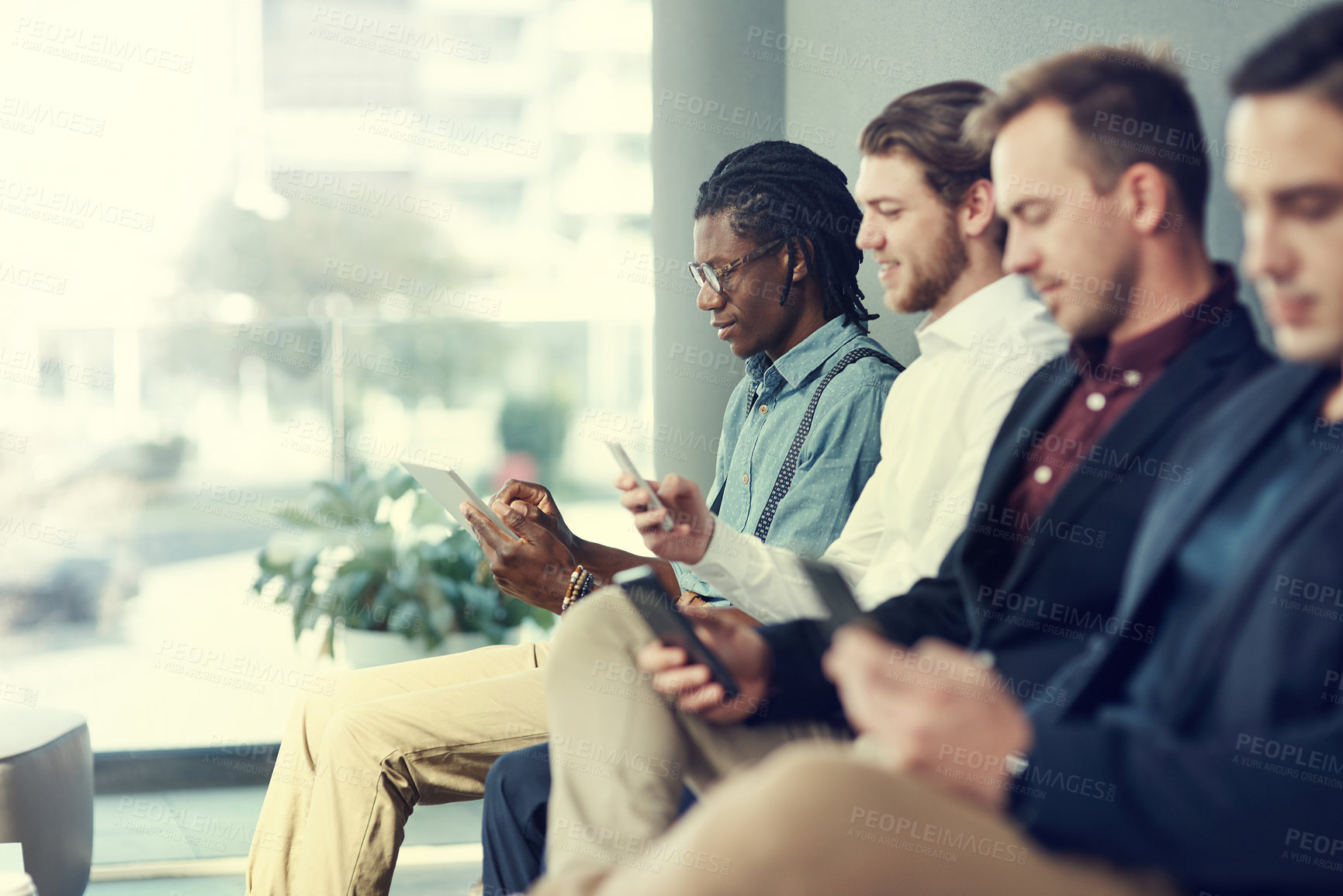 Buy stock photo Shot of a group of businessmen using different wireless devices while waiting in line for an interview