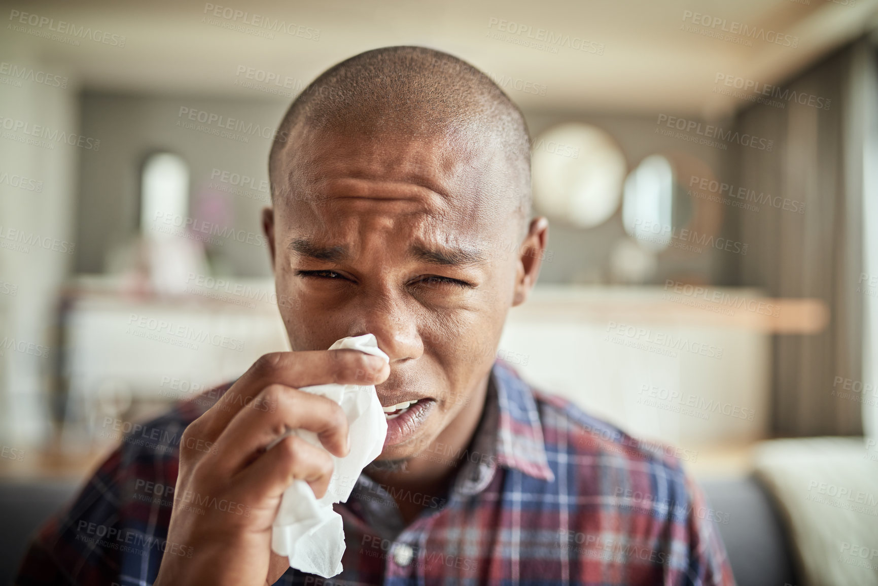 Buy stock photo Portrait of an uncomfortable looking young man holding a tissue in front of his nose while being seated on a couch at home