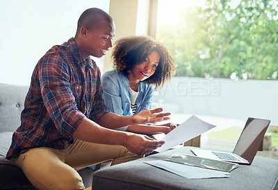 Buy stock photo Shot of a cheerful young couple working on a laptop and doing paperwork together while being seated on a couch at home