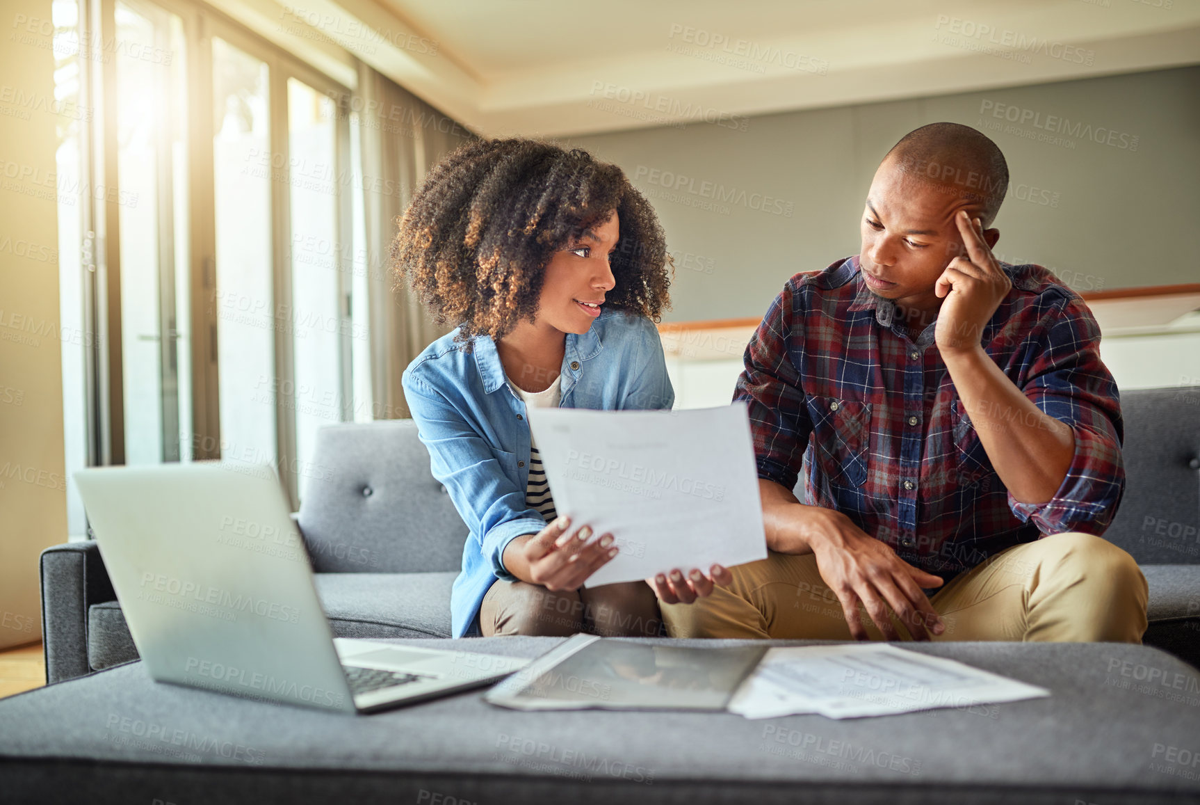 Buy stock photo Shot of a focused young couple working on a laptop and doing paperwork together while being seated on a couch at home