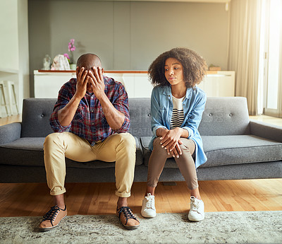 Buy stock photo Shot of a stressed out young couple seated on a couch together while contemplating at home during the day