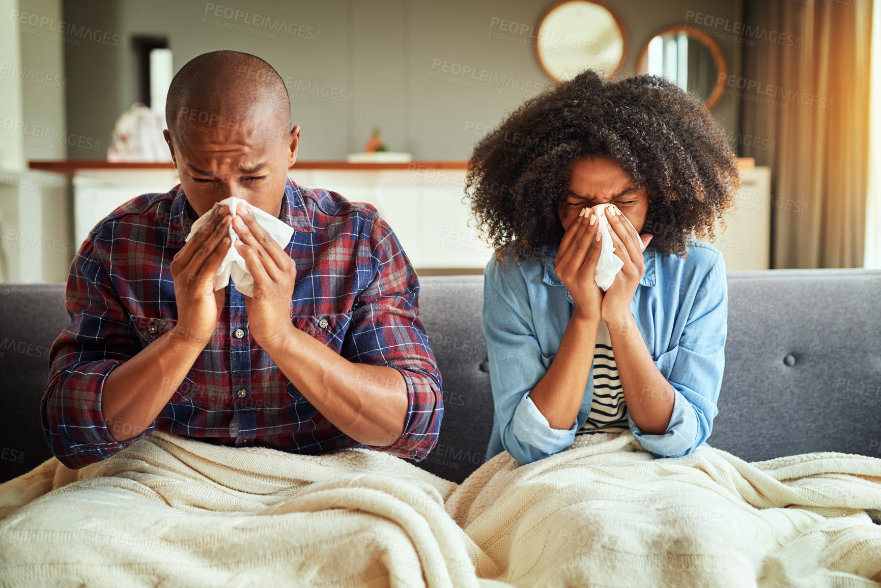 Buy stock photo Shot of a tired looking young couple seated on a couch with blankets while being sick together at home