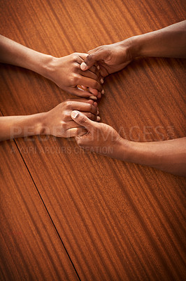 Buy stock photo High angle shot of two unrecognizable people's hands holding each other while resting on top of a wooden table