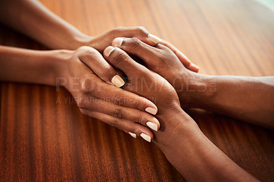 Buy stock photo Closeup of two unrecognizable people's hands holding each other while resting on top of a wooden table