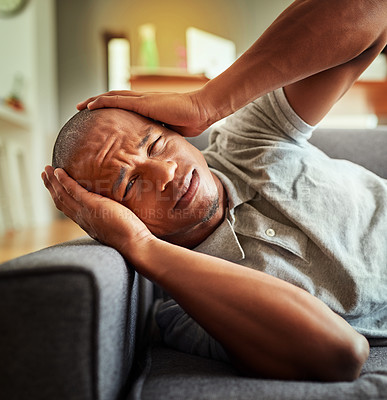 Buy stock photo Shot of a stressed out young man lying on a couch while holding his head in discomfort inside at home during the day
