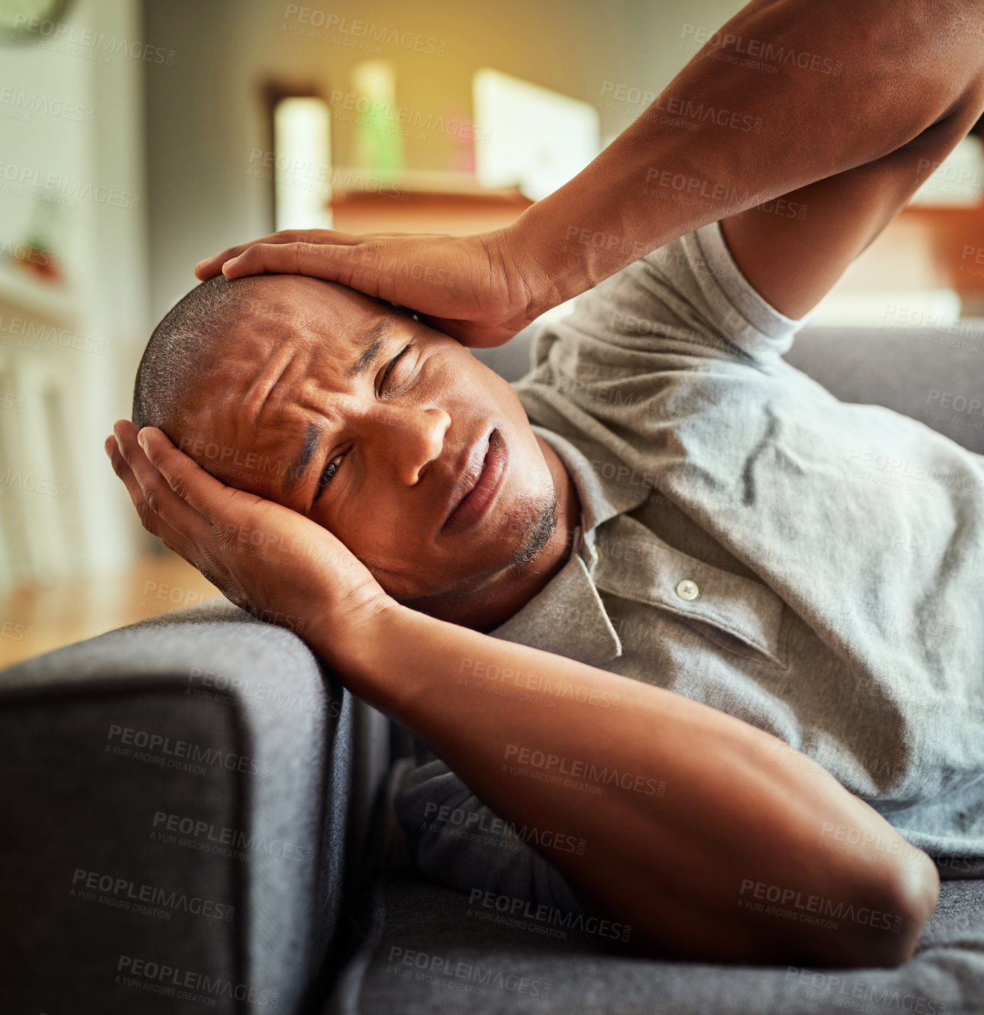 Buy stock photo Shot of a stressed out young man lying on a couch while holding his head in discomfort inside at home during the day