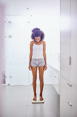 Buy stock photo Shot of an attractive young woman weighing herself on a scale in the bathroom at home