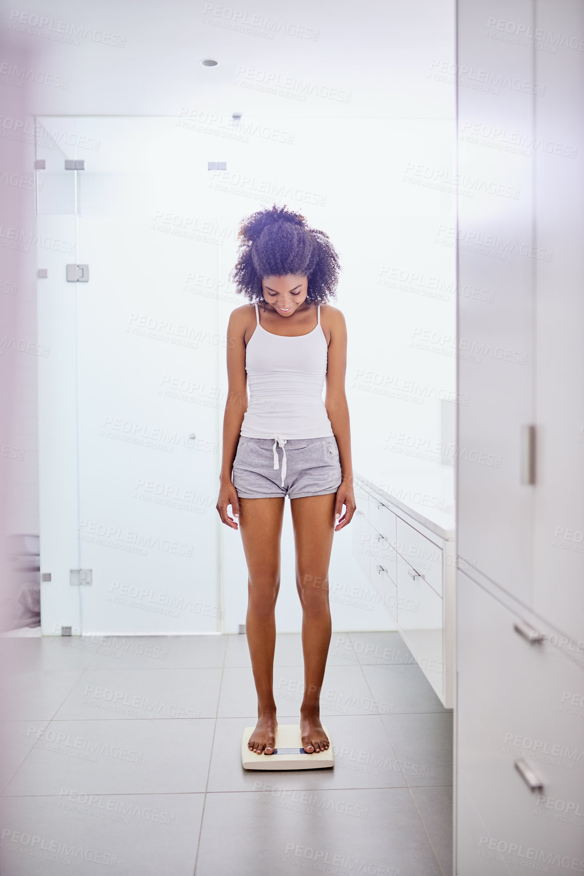 Buy stock photo Shot of an attractive young woman weighing herself on a scale in the bathroom at home