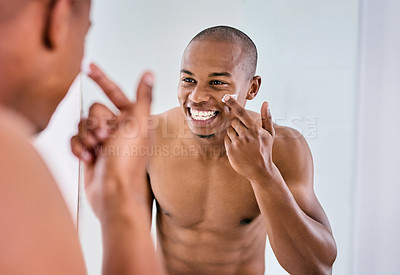 Buy stock photo Shot of a handsome young man applying moisturizer to his face in the bathroom at home