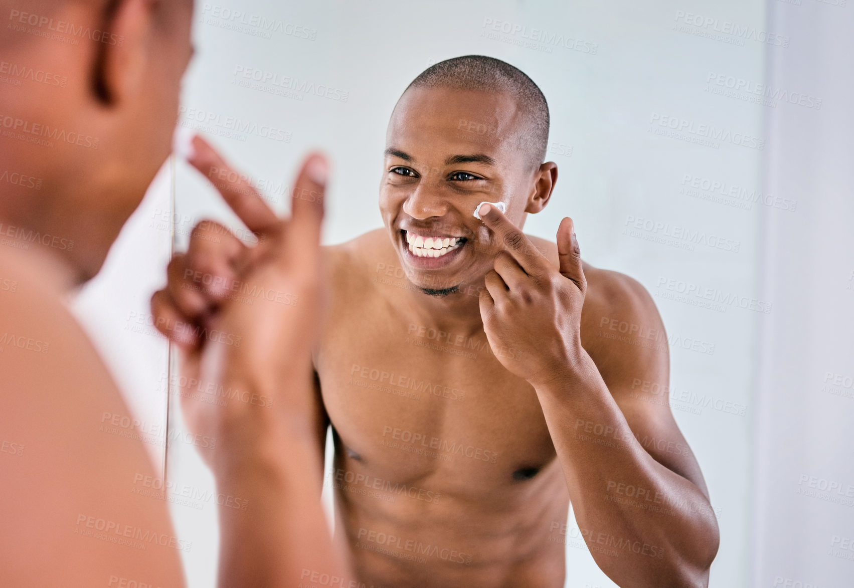 Buy stock photo Shot of a handsome young man applying moisturizer to his face in the bathroom at home