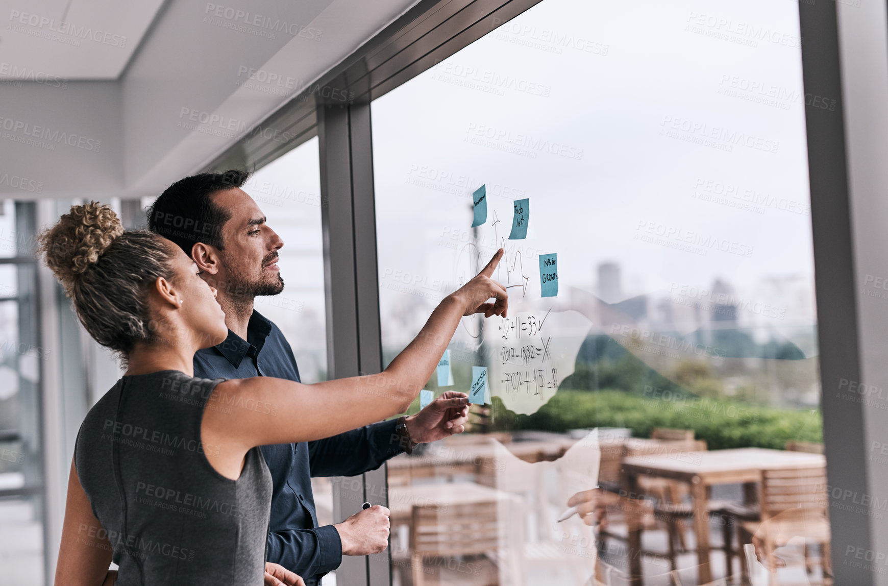 Buy stock photo Shot of two businesspeople brainstorming on a glass wall in an office