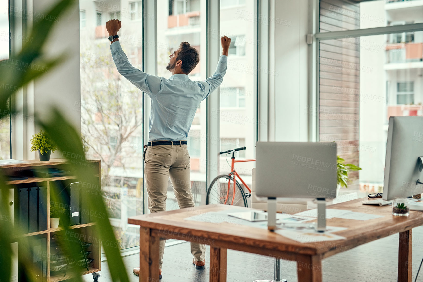 Buy stock photo Rearview shot of a businessman cheering while standing at a window in an office