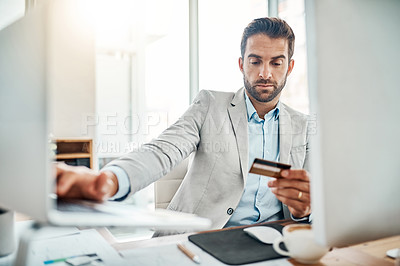 Buy stock photo Shot of a handsome young businessman using a computer while holding a credit card in an office