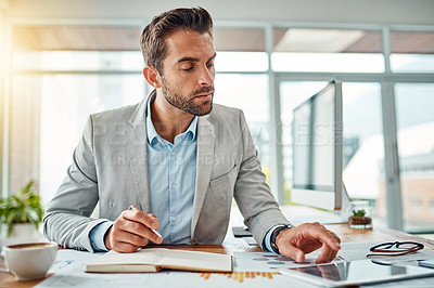 Buy stock photo Shot of a handsome young businessman writing notes while using a digital tablet in an office