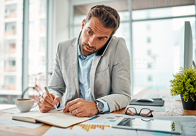 Buy stock photo Shot of a handsome young businessman writing notes while talking on a cellphone in an office