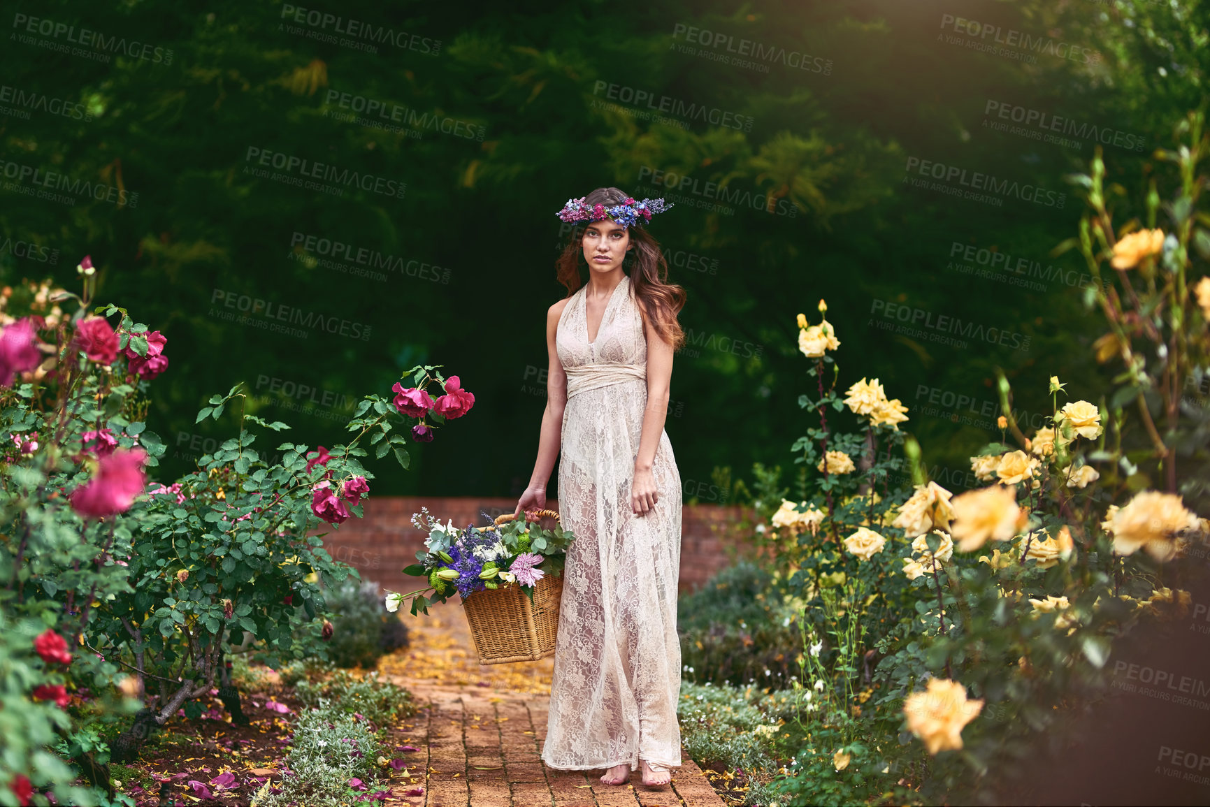 Buy stock photo Shot of a beautiful young woman wearing a floral head wreath and holding a basket full of flowers in nature