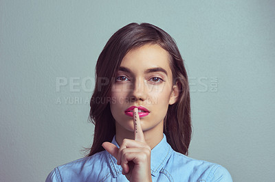 Buy stock photo Studio portrait of an attractive young woman posing with her finger on lips against a grey background