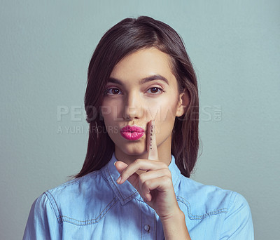 Buy stock photo Studio portrait of an attractive young woman posing with her finger on lips against a grey background