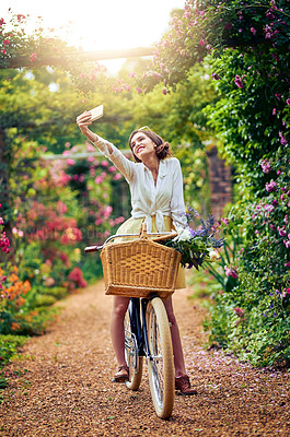 Buy stock photo Shot of an attractive young woman taking a selfie while riding a bicycle outdoors