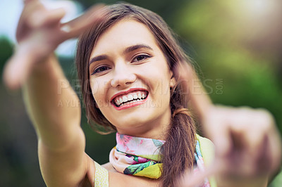 Buy stock photo Portrait of a cheerful young woman making a frame shape with her hands while looking at the camera outside during the day