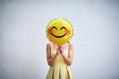 Buy stock photo Studio shot of a young woman holding a balloon with a smiley in front of her face