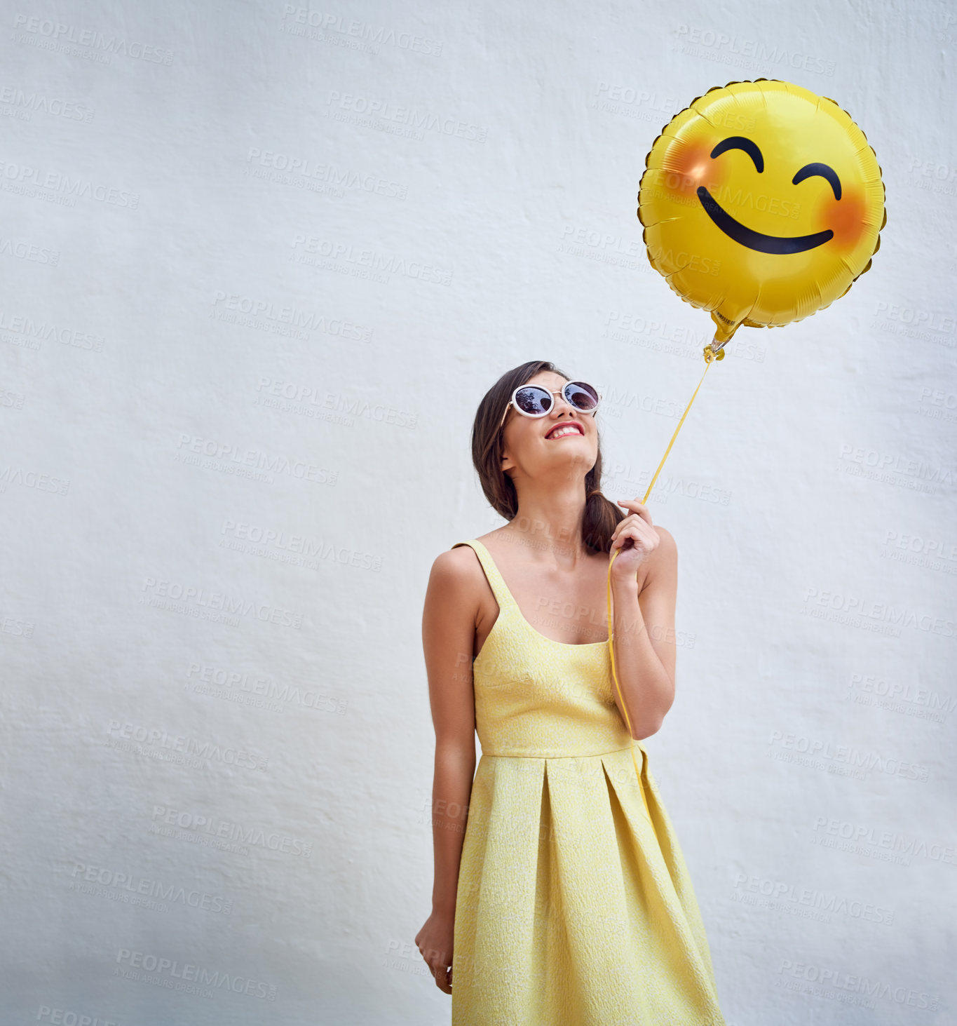 Buy stock photo Woman, balloon and happy by wall in with emoji, smile and face for fashion sunglasses at party, event or celebration. Gen z and girl and excited with icon, space and yellow dress to celebrate spring