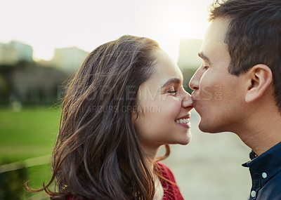 Buy stock photo Shot of a young man kissing his girlfriend on the nose outdoors