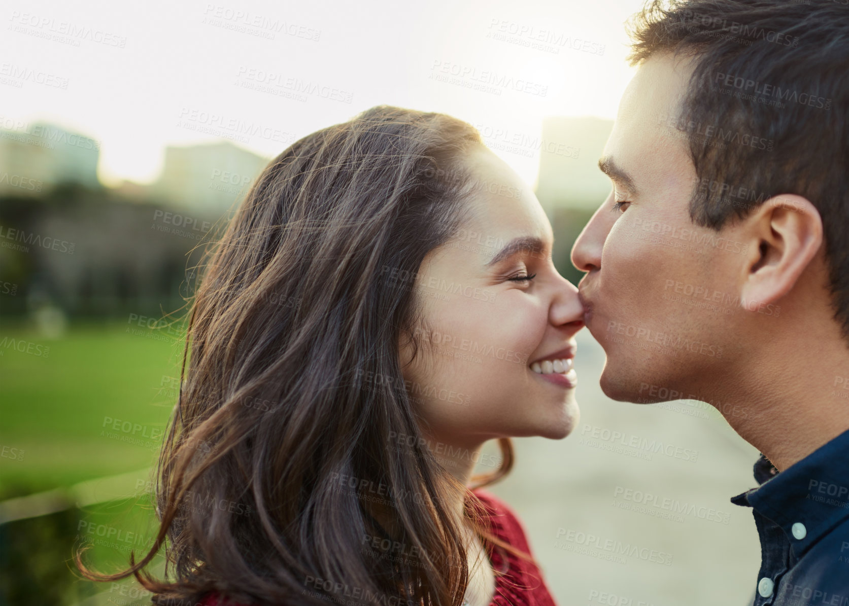 Buy stock photo Shot of a young man kissing his girlfriend on the nose outdoors