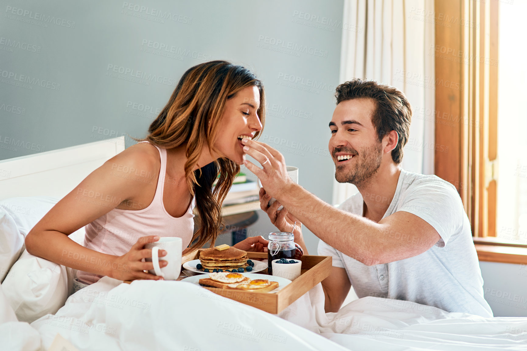 Buy stock photo Shot of a happy young couple enjoying breakfast in bed together at home