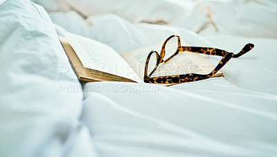 Buy stock photo Still life shot of a book and a pair of spectacles on a bed